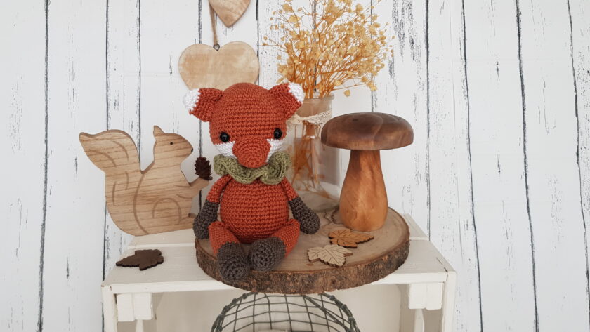 tommy the fox sitting next to a wooden mushroom and a wooden squirrel