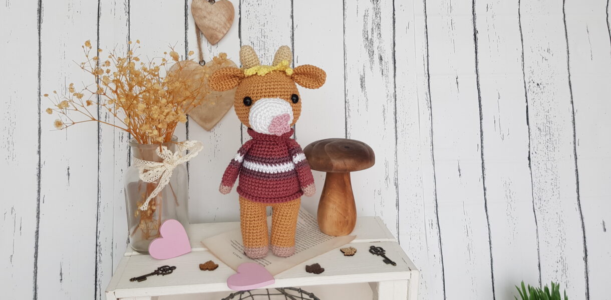 Crochet cow standing on a nice shelf with wooden mushroom toy and flowers