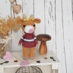 Crochet cow standing on a nice shelf with wooden mushroom toy and flowers