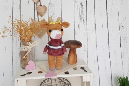 Crochet cow standing on a nice shelf with wooden mushroom toy and flowers