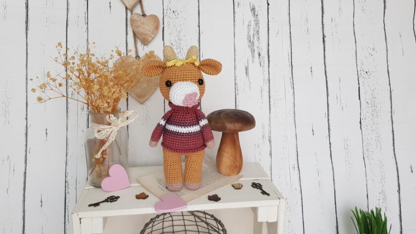 Crochet cow standing on a nice shelf with wooden mushroom toy and flowers