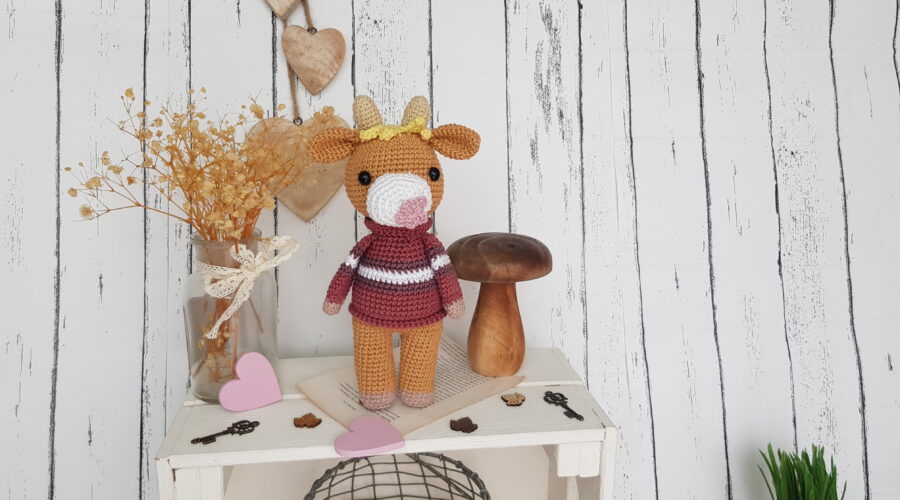 Crochet cow standing on a nice shelf with wooden mushroom toy and flowers