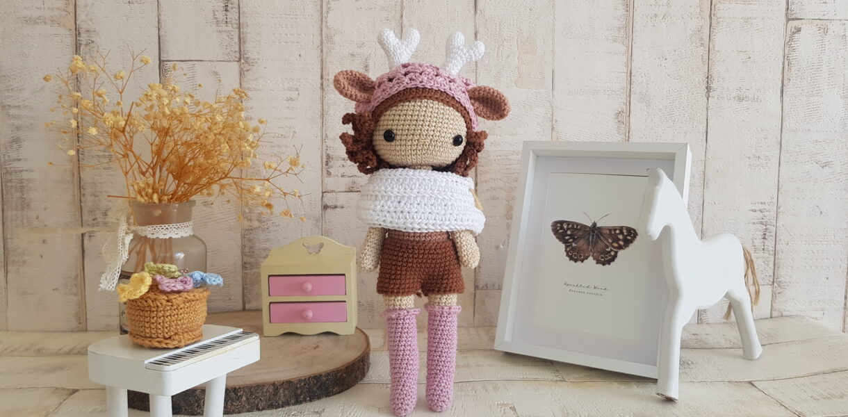 crochet deer girl doll standing next to a piano, a rocking horse and a nice painting