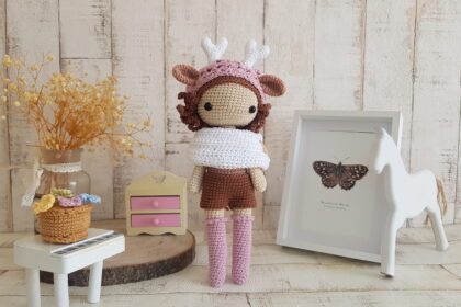 crochet deer girl doll standing next to a piano, a rocking horse and a nice painting