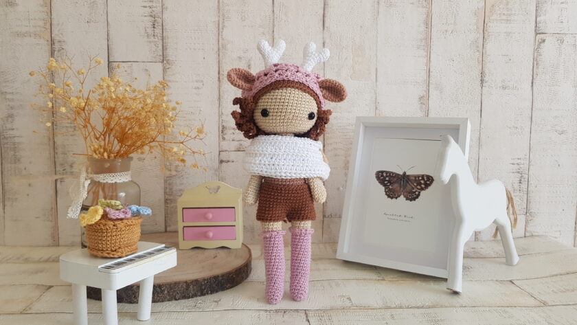 crochet deer girl doll standing next to a piano, a rocking horse and a nice painting