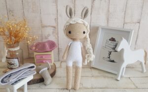 crochet doll with bunny ears and long hair standing next to a toy piano