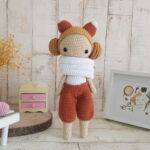 crochet doll with fox ears standing next toa piano, a rocking horse and a nice painting