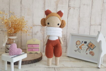 crochet doll with fox ears standing next toa piano, a rocking horse and a nice painting