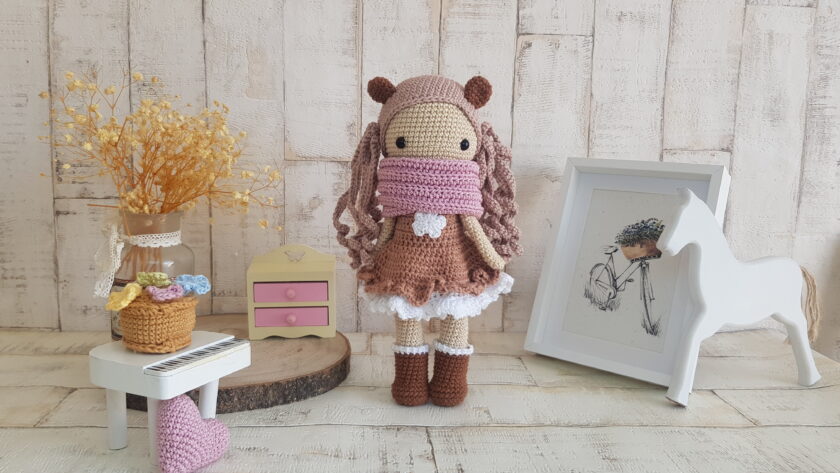 crochet doll standing next to a piano, a rocking horse and a nice painting