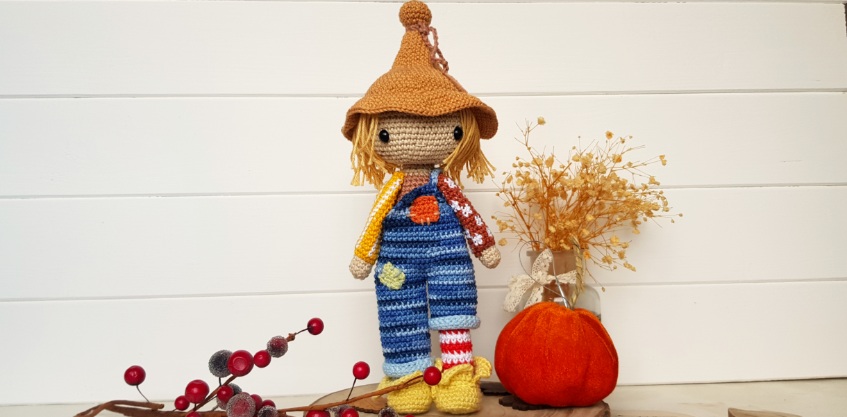 crochet scarecrow standing next to a pumpkin and flowers