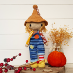 crochet scarecrow standing next to a pumpkin and flowers