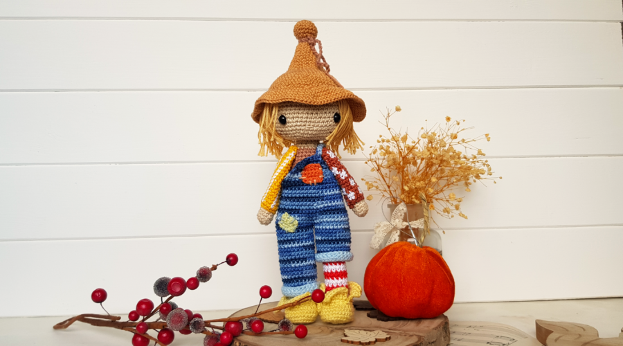 crochet scarecrow standing next to a pumpkin and flowers