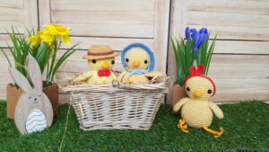 3 crochet chickens sitting on the grass and in a basket